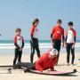Moniteur de surf sur la plage et élèves en combinaison