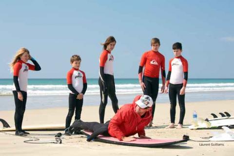 Moniteur de surf sur la plage et élèves en combinaison