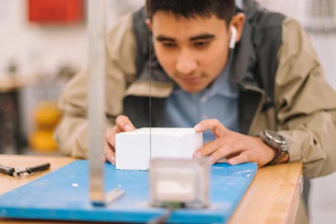 Une formation théorique et pratique Etudiant sciant un bloc