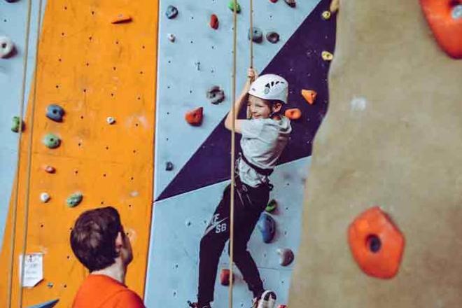 Jeune sur un mur d&#039;escalade encadré par un éducateur sportif