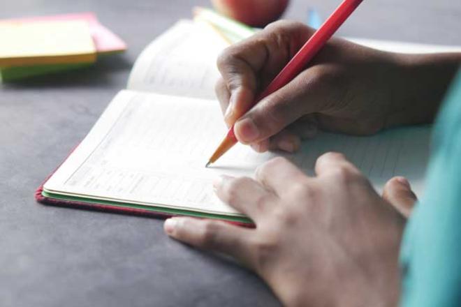 Un calendrier pour anticiper les étapes Main d'élève qui remplit un agenda